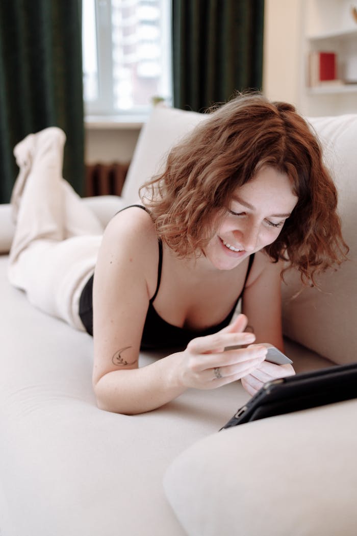 A woman on a couch happily shops online using a tablet and credit card, enjoying the convenience of e-commerce at home.